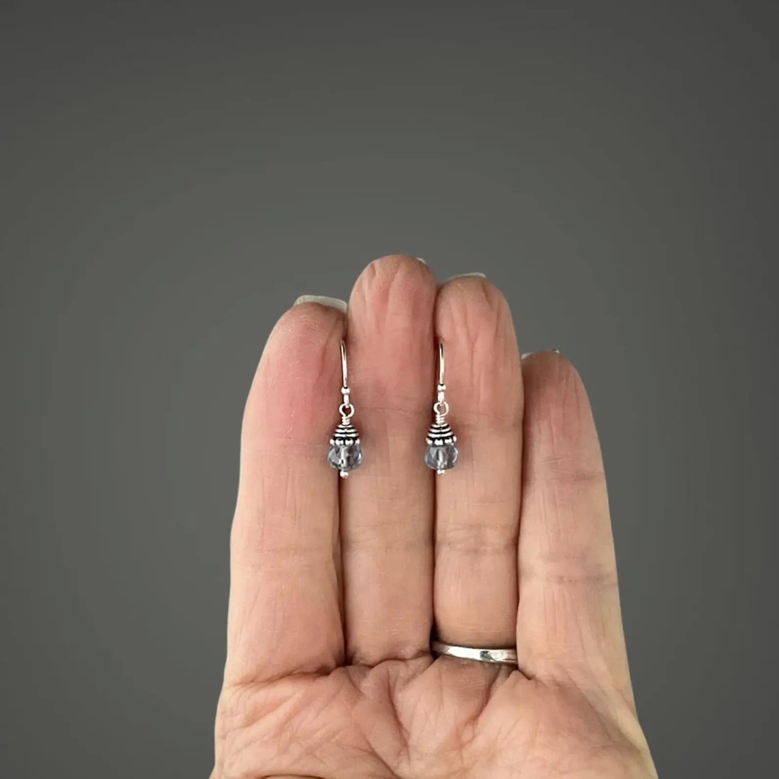 Silver earrings held between fingers against a gray background
