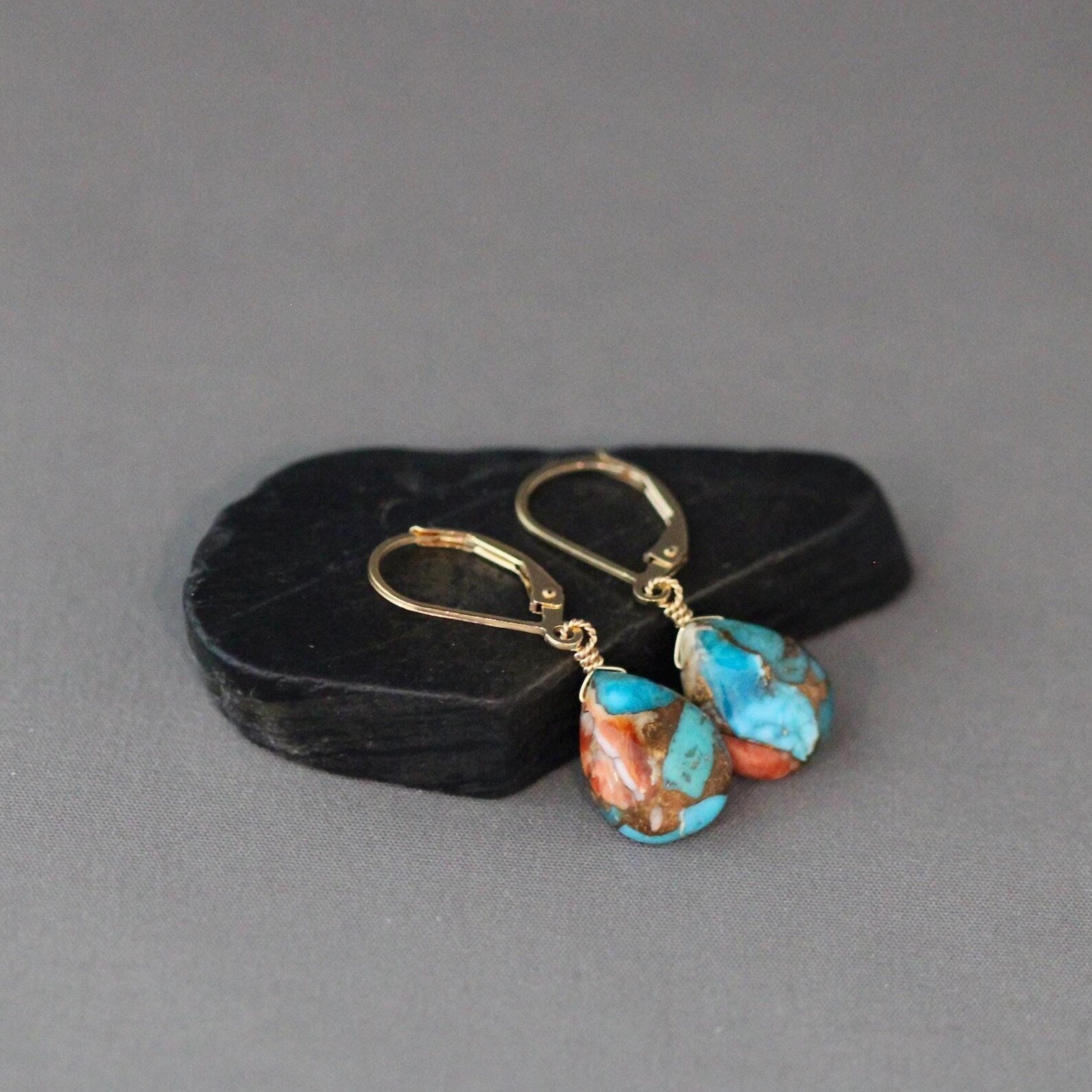 Turquoise and gold earrings on a gray background
