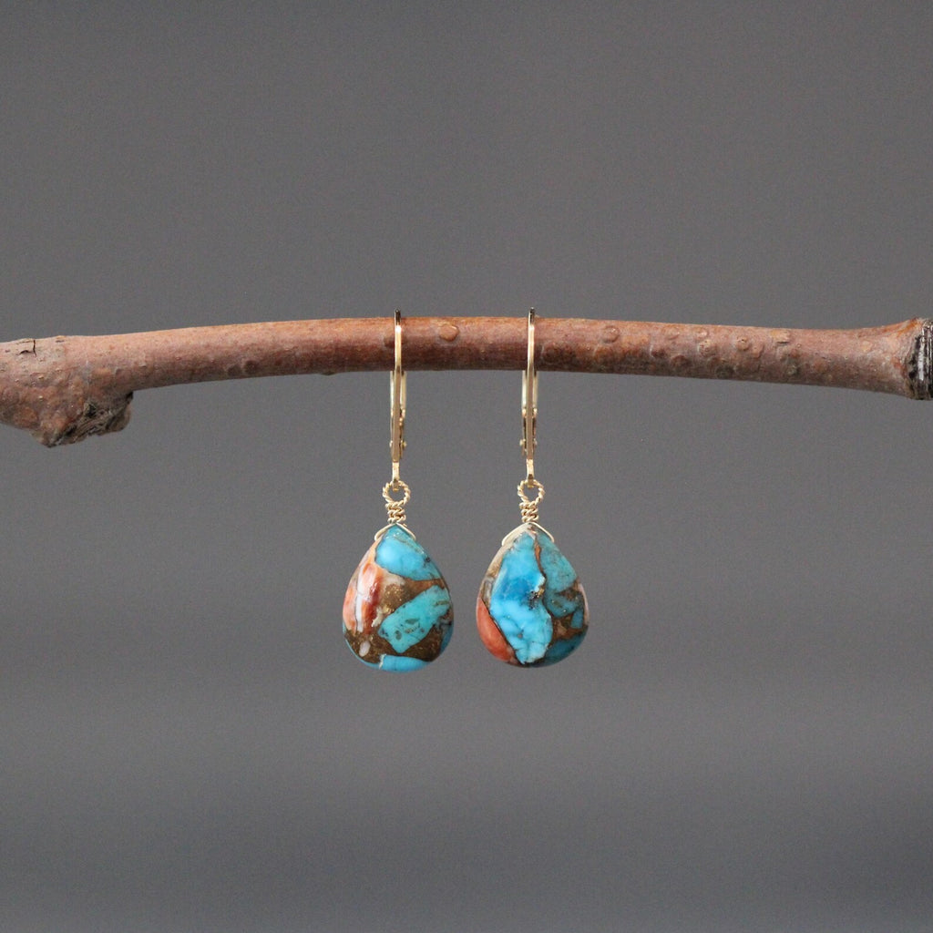 Turquoise teardrop earrings hanging on a branch against a gray background