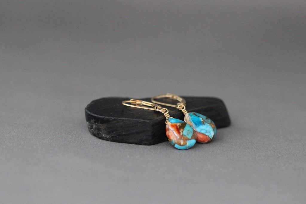 Pair of earrings with turquoise stones and gold earwires on a gray background