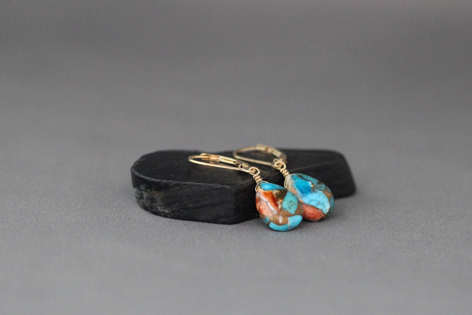 Pair of earrings with turquoise stones and gold earwires on a gray background