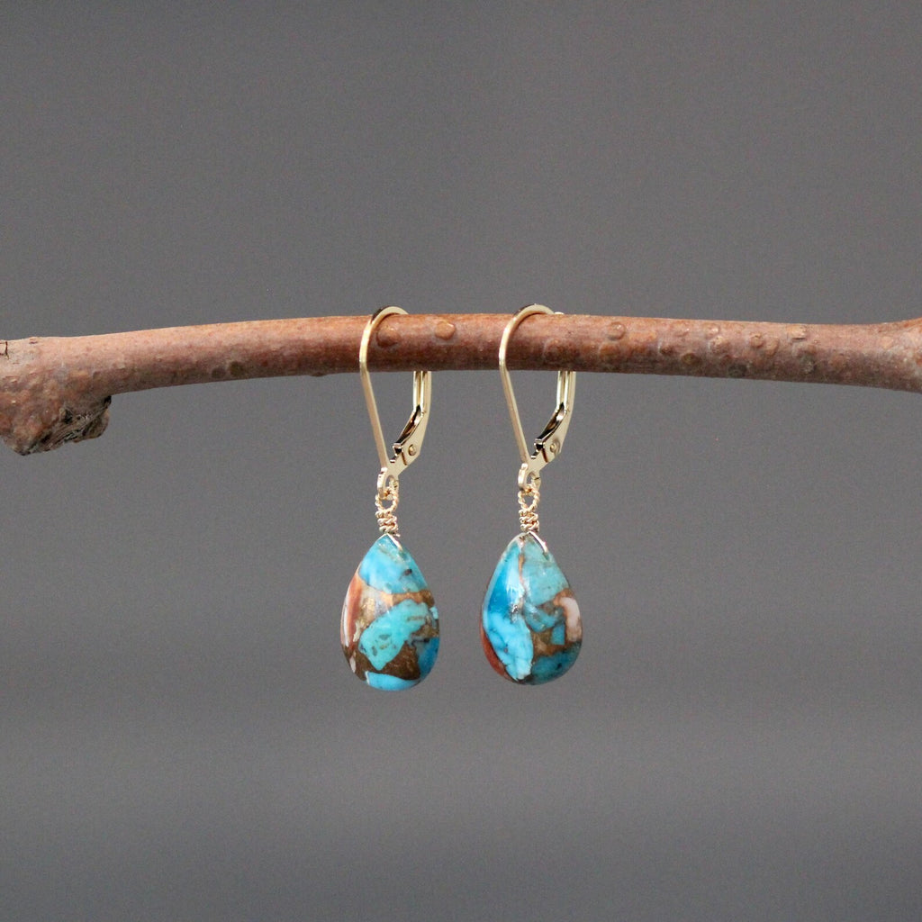 Turquoise teardrop earrings on a branch with a gray background