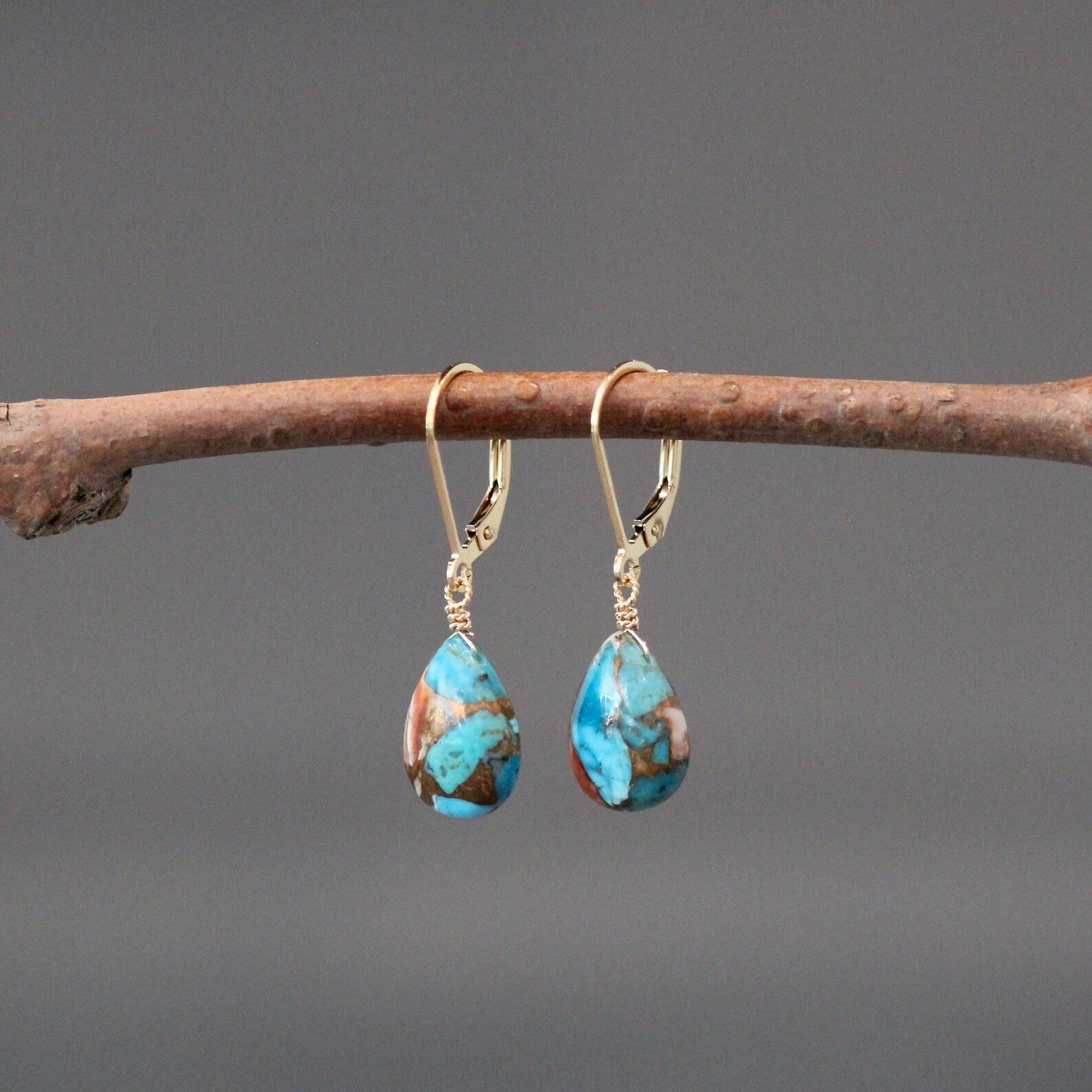 Turquoise teardrop earrings on a branch with a gray background
