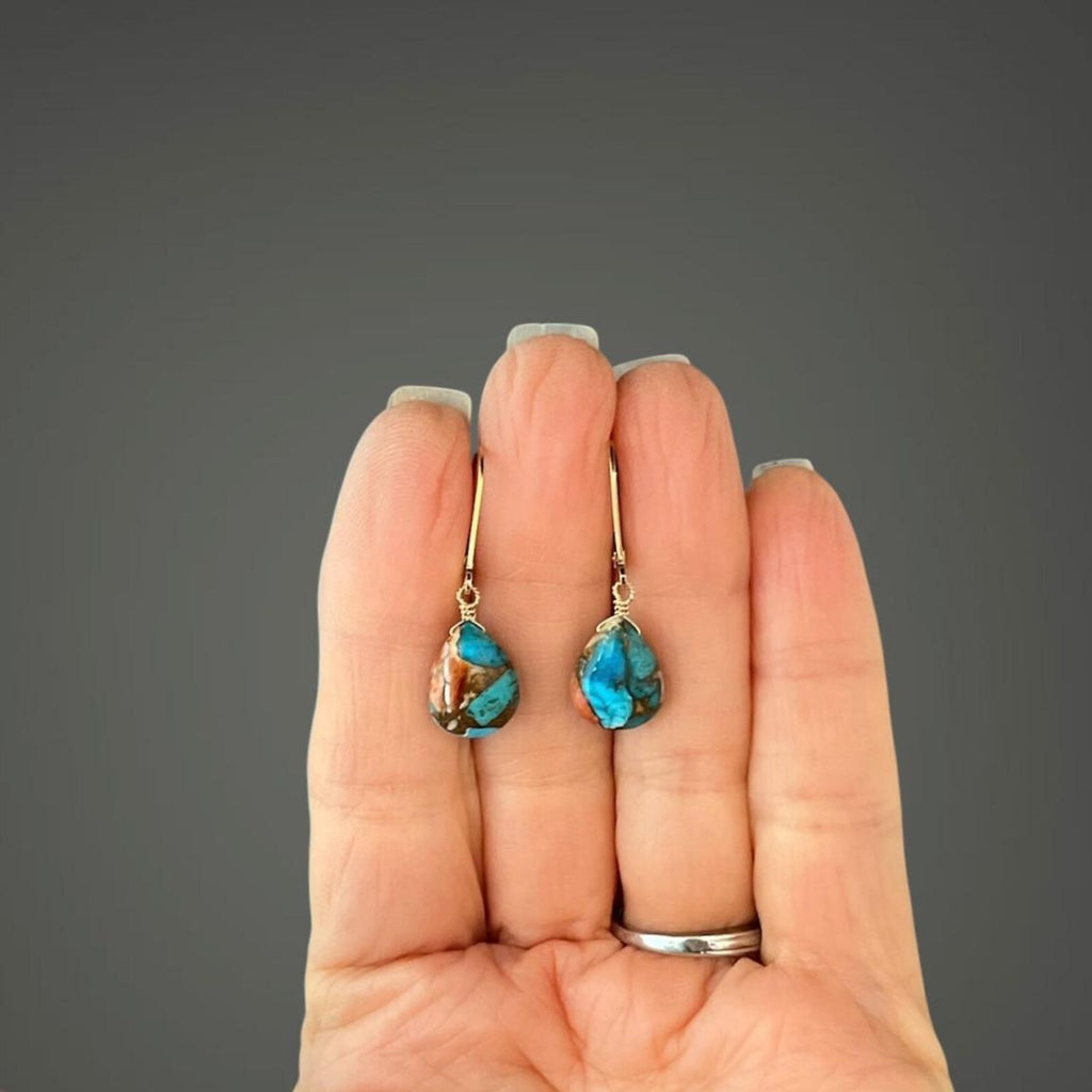 Turquoise earrings held in a hand against a gray background