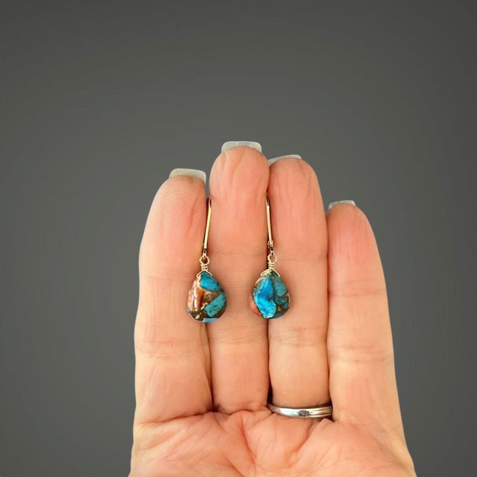 Turquoise earrings held in a hand against a gray background