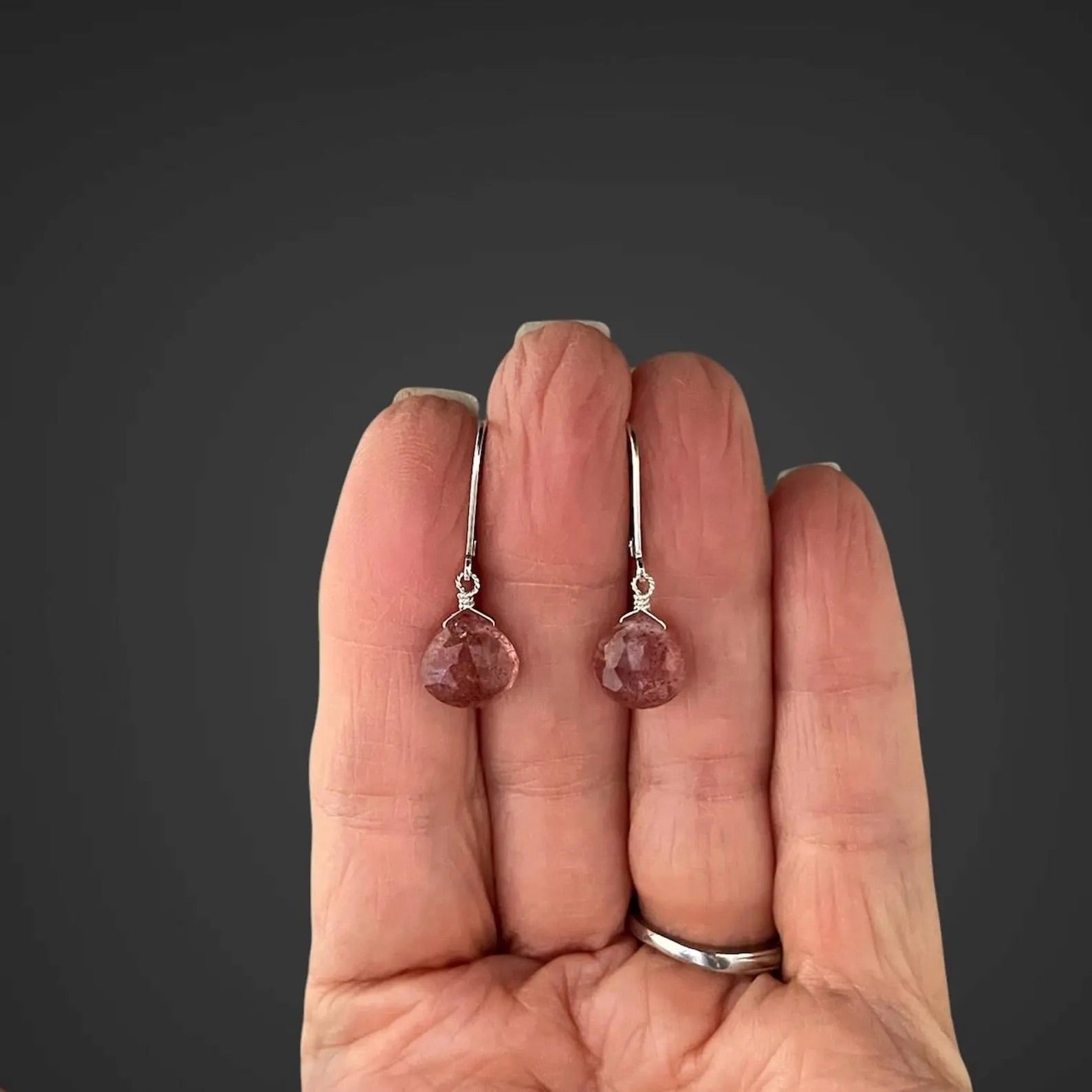 Strawberry quartz and silver earrings held in the palm of a person's hand